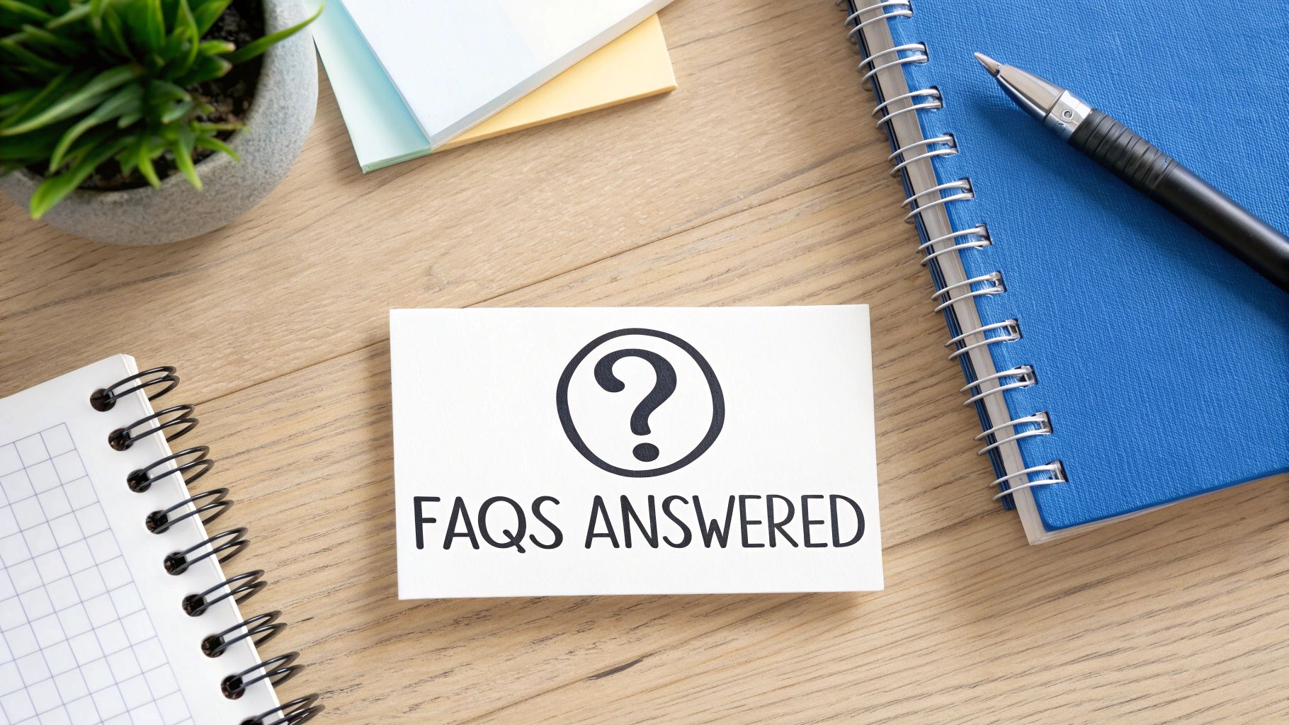 FAQs answered card on wooden desk with notebooks pen and plant